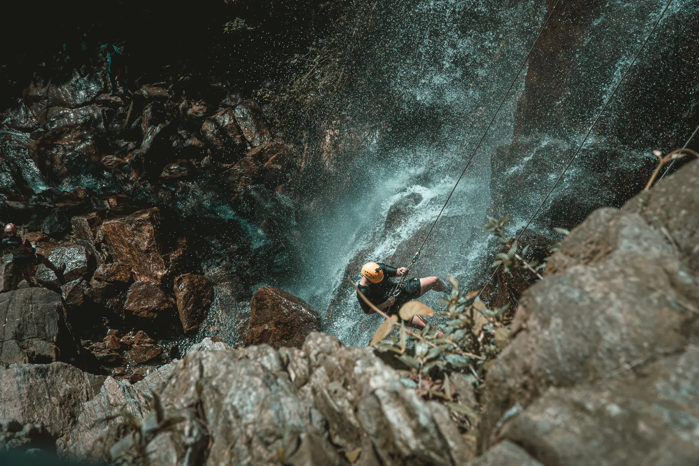 Participant en canyoning descendant une paroi rocheuse sous une cascade
